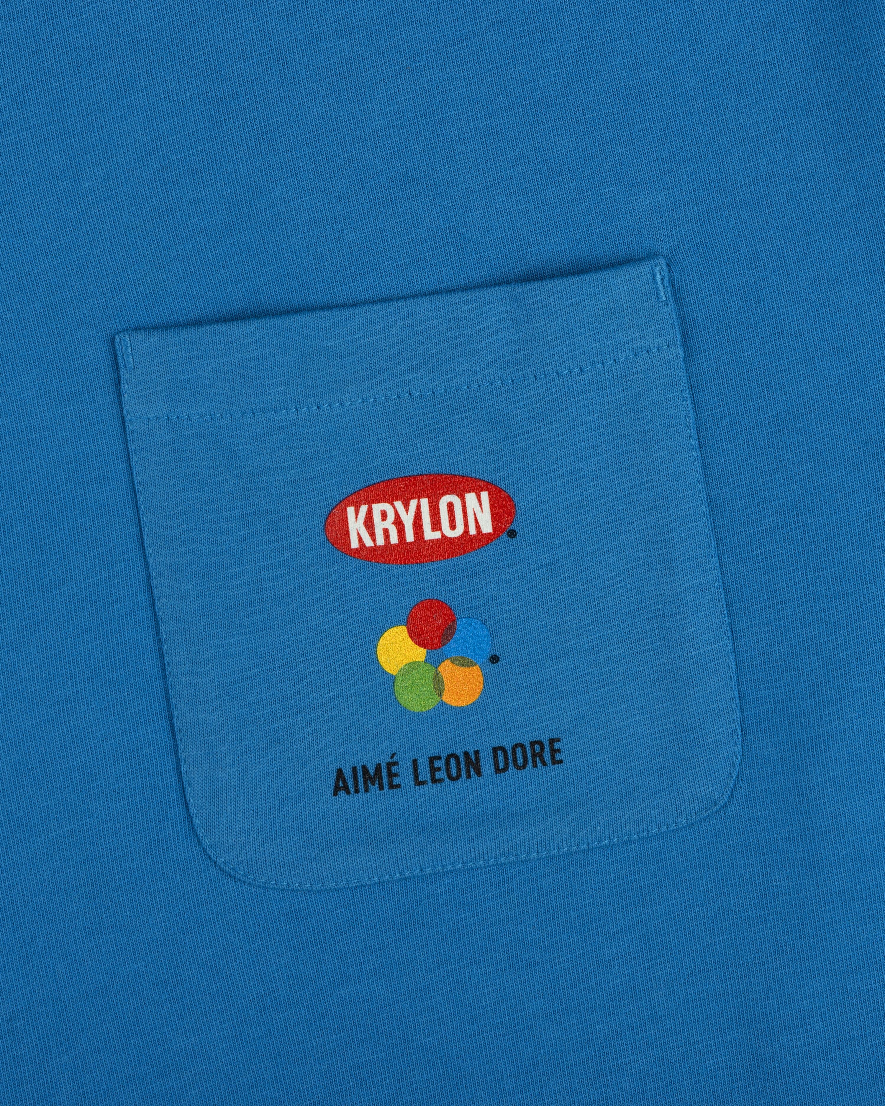 Krylon Pocket Tee: blue shirt with KRYLON logo, colorful paint blobs, and AIMÉ LEON DORE below the pocket.