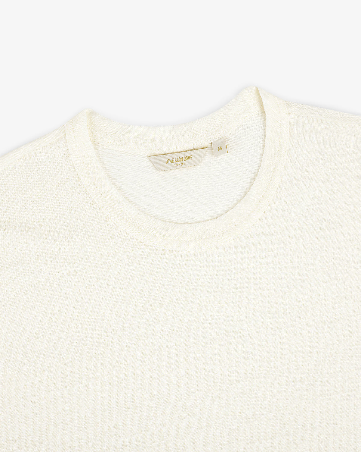 Close-up of the Linen Tee, a plain off-white crew neck T-shirt laid flat on a white background.
