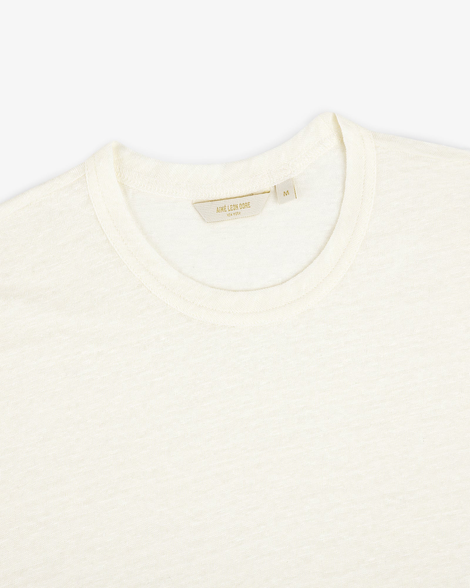 Close-up of the Linen Tee, a plain off-white crew neck T-shirt laid flat on a white background.