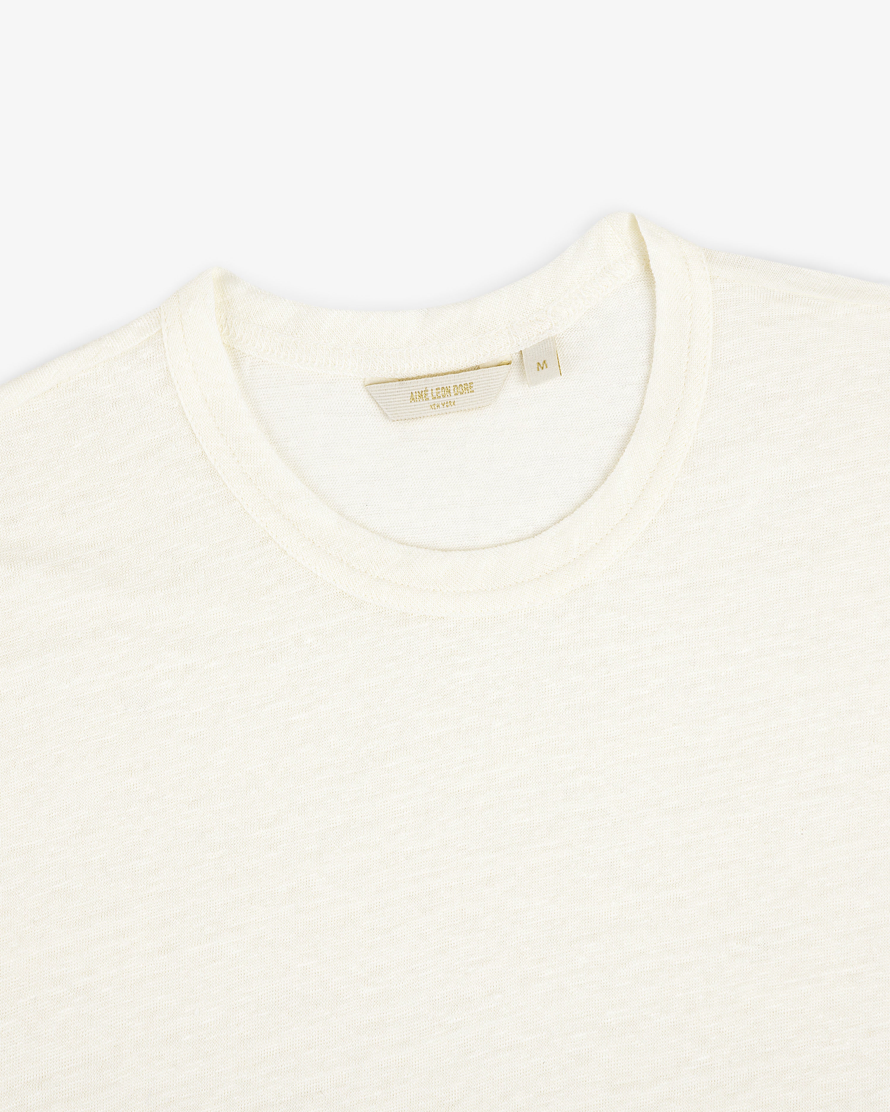 Close-up of the Linen Tee, a plain off-white crew neck T-shirt laid flat on a white background.