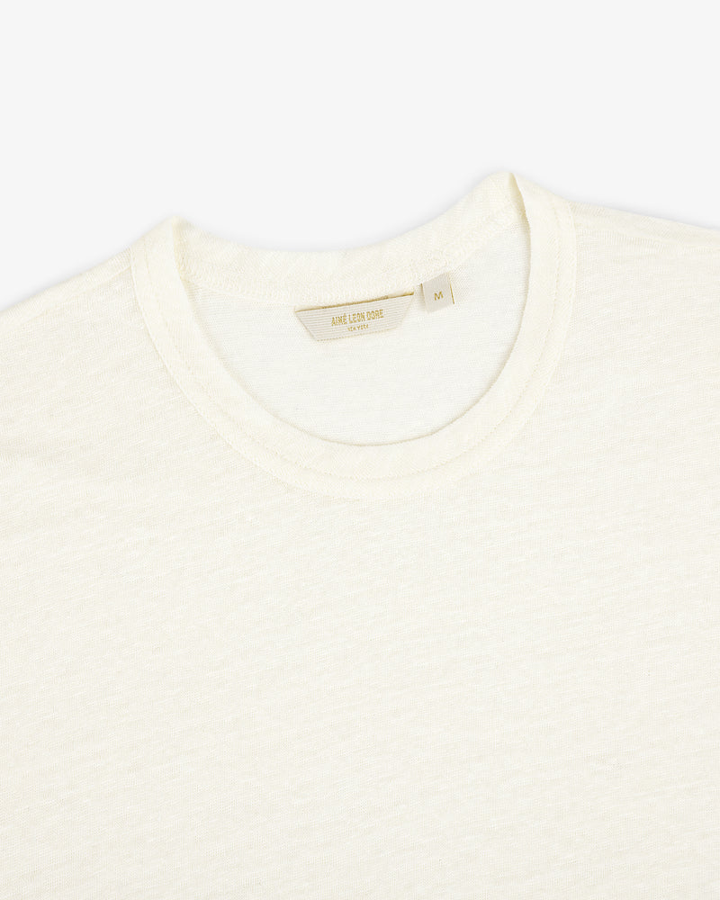 Close-up of the Linen Tee, a plain off-white crew neck T-shirt laid flat on a white background.