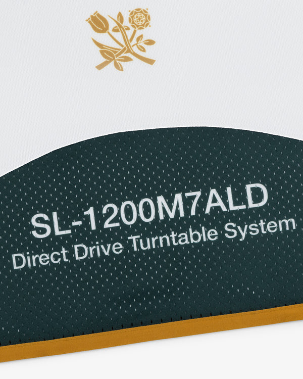 Close-up of ALD / Technics Soccer Jersey on black and white fabric with a gold floral emblem.