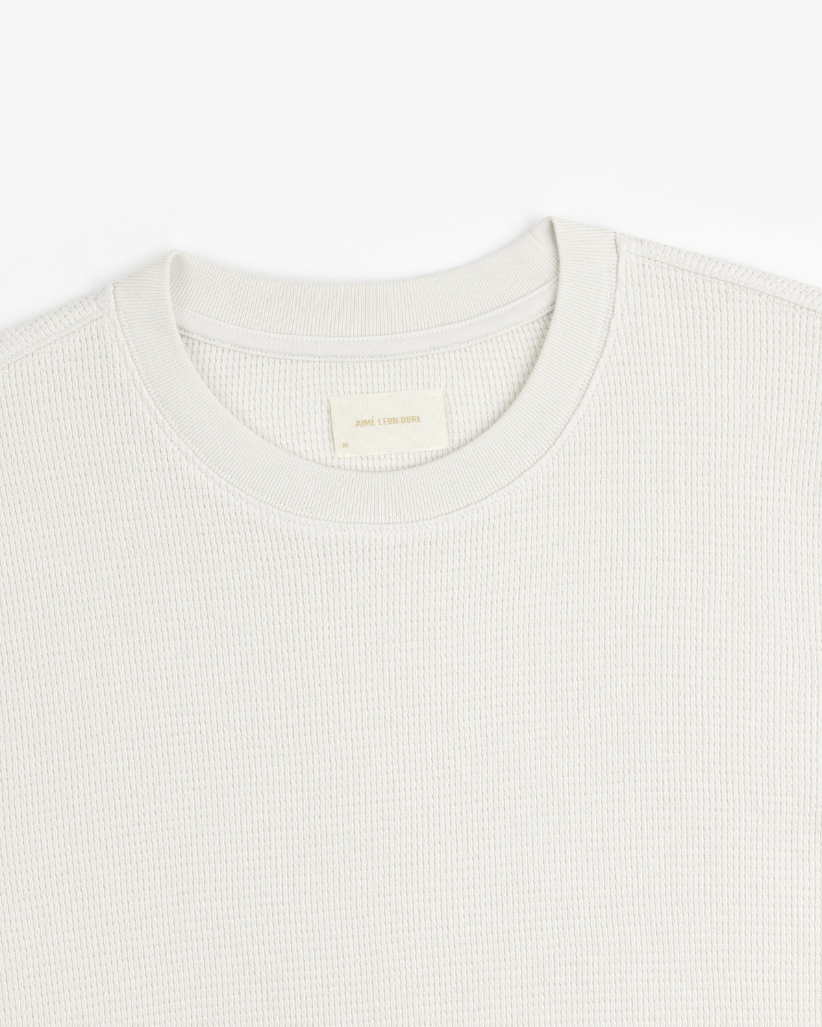 Close-up of a textured off-white Long-Sleeve Waffle Thermal with a woven label at the crewneck.