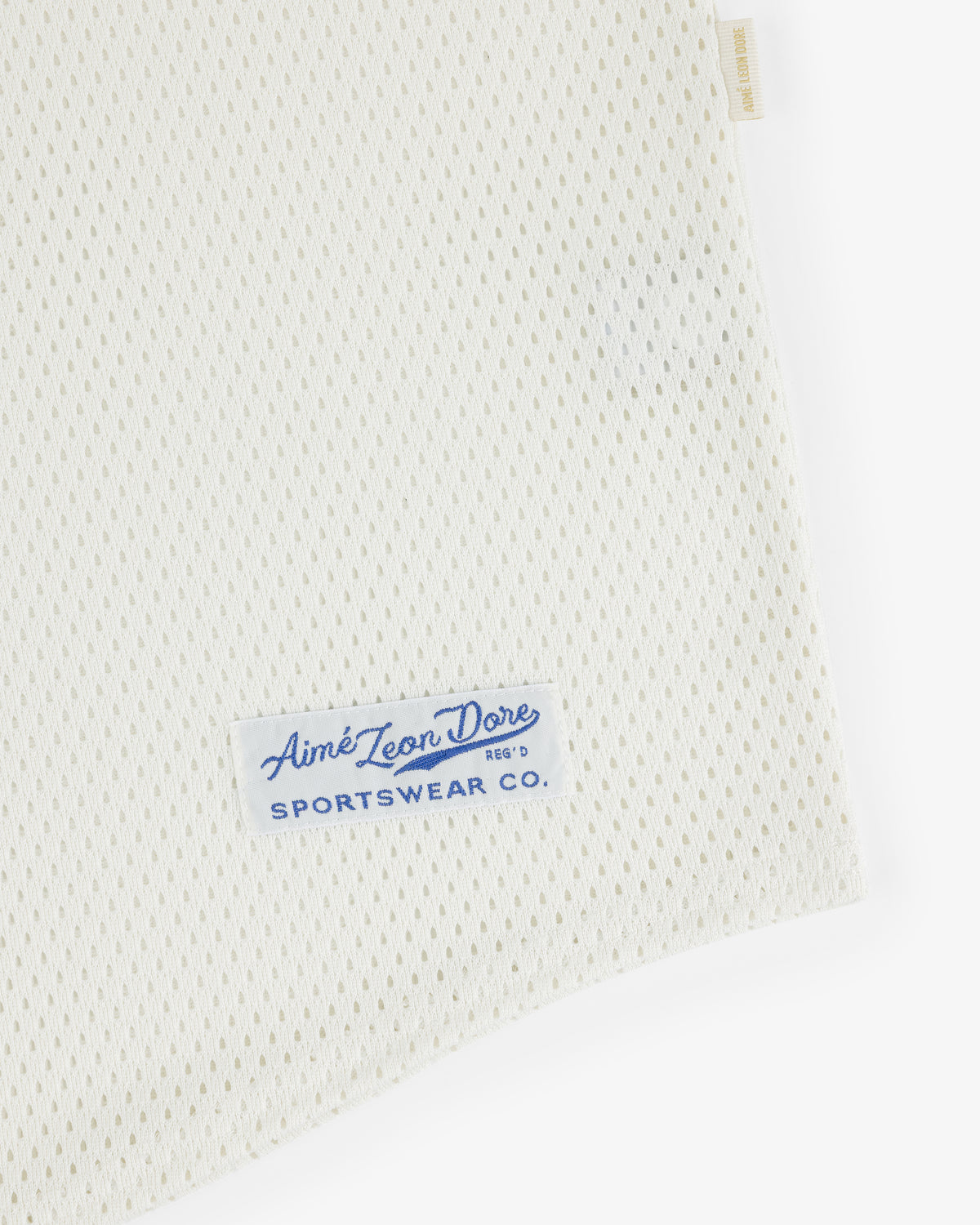 Close-up of white Mesh Batting Practice Jersey with a blue Aimé Leon Dore Sportswear Co. label sewn on.