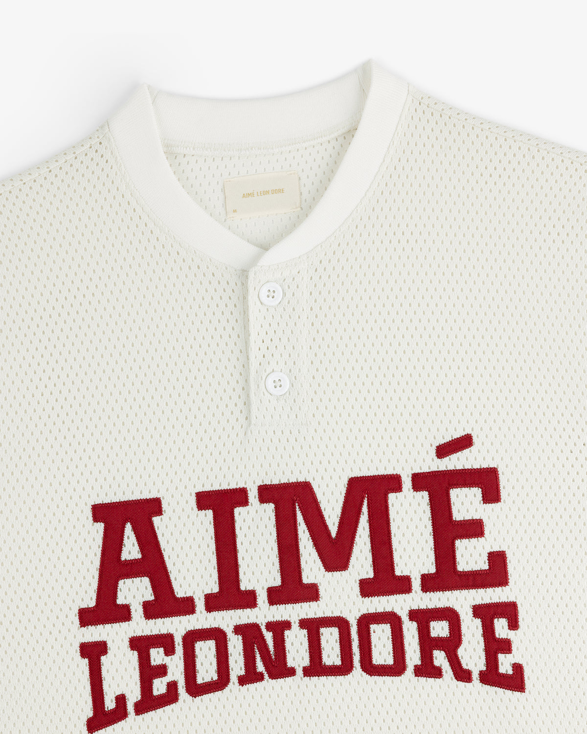 Close-up of a white Mesh Batting Practice Jersey with AIMÉ LEON DORE in bold red letters and two collar buttons.