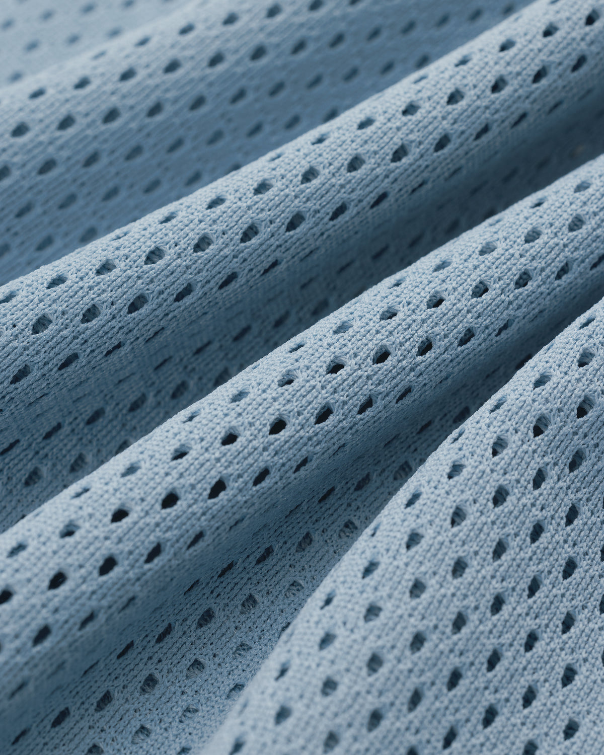 Close-up of Mesh Batting Practice Jersey featuring light blue perforated fabric with wavy folds and small holes.