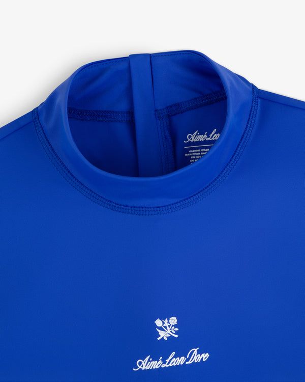 Blue Short Sleeve Crest Rash Guard with “Aimé Leon Dore” and a small white rose logo embroidered on the chest.