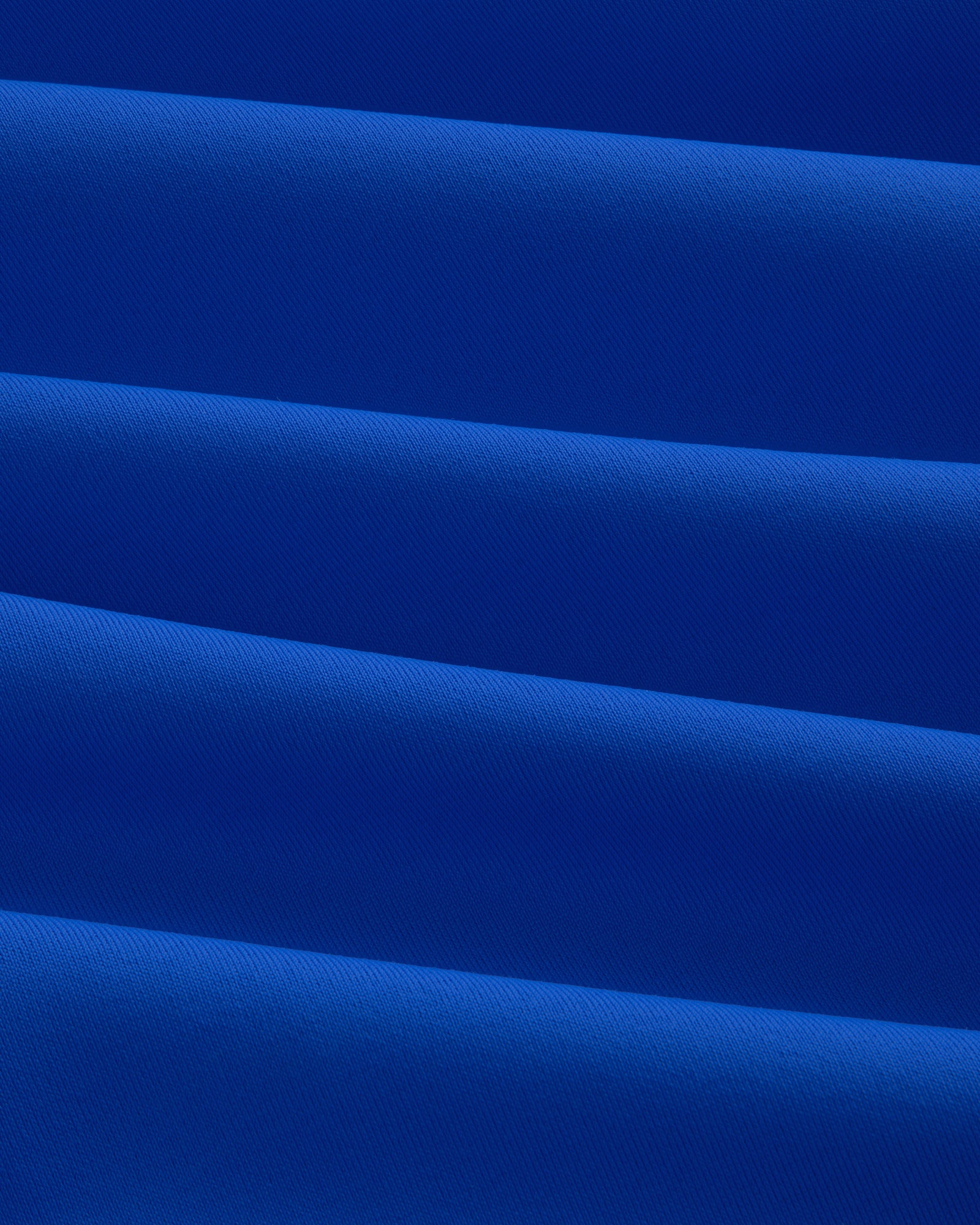 Close-up of folded, smooth royal blue Short Sleeve Crest Rash Guard with diagonal pleats and subtle texture.