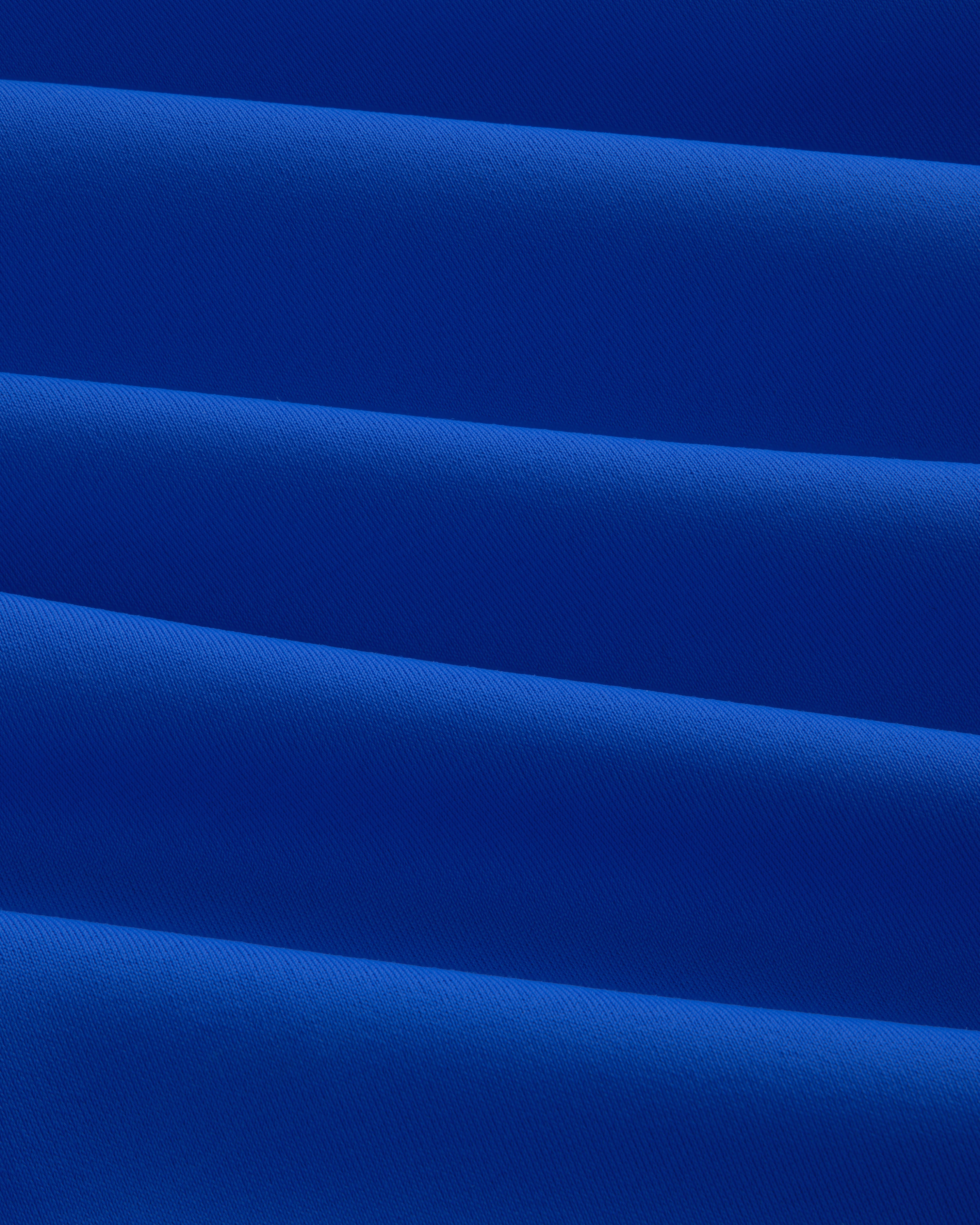 Close-up of folded, smooth royal blue Short Sleeve Crest Rash Guard with diagonal pleats and subtle texture.