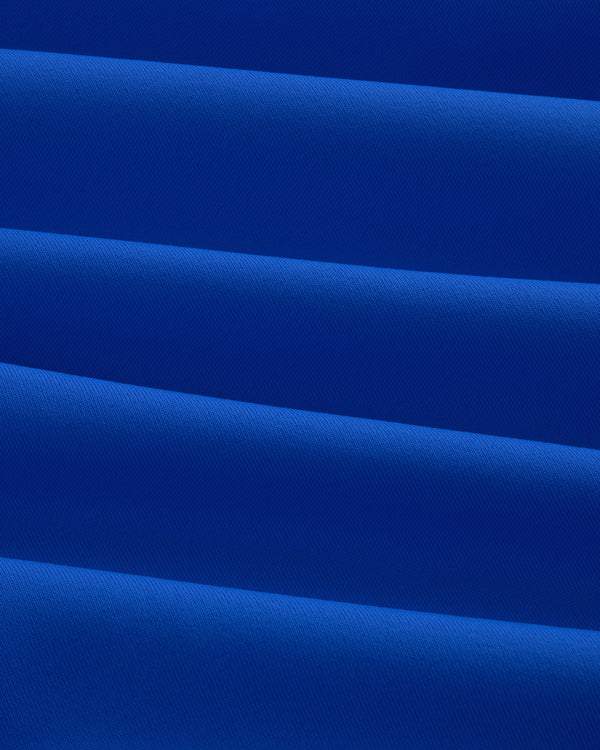 Close-up of folded, smooth royal blue Short Sleeve Crest Rash Guard with diagonal pleats and subtle texture.