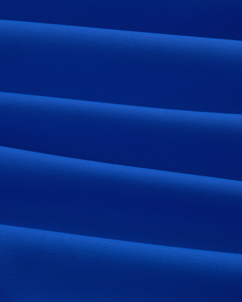 Close-up of folded, smooth royal blue Short Sleeve Crest Rash Guard with diagonal pleats and subtle texture.