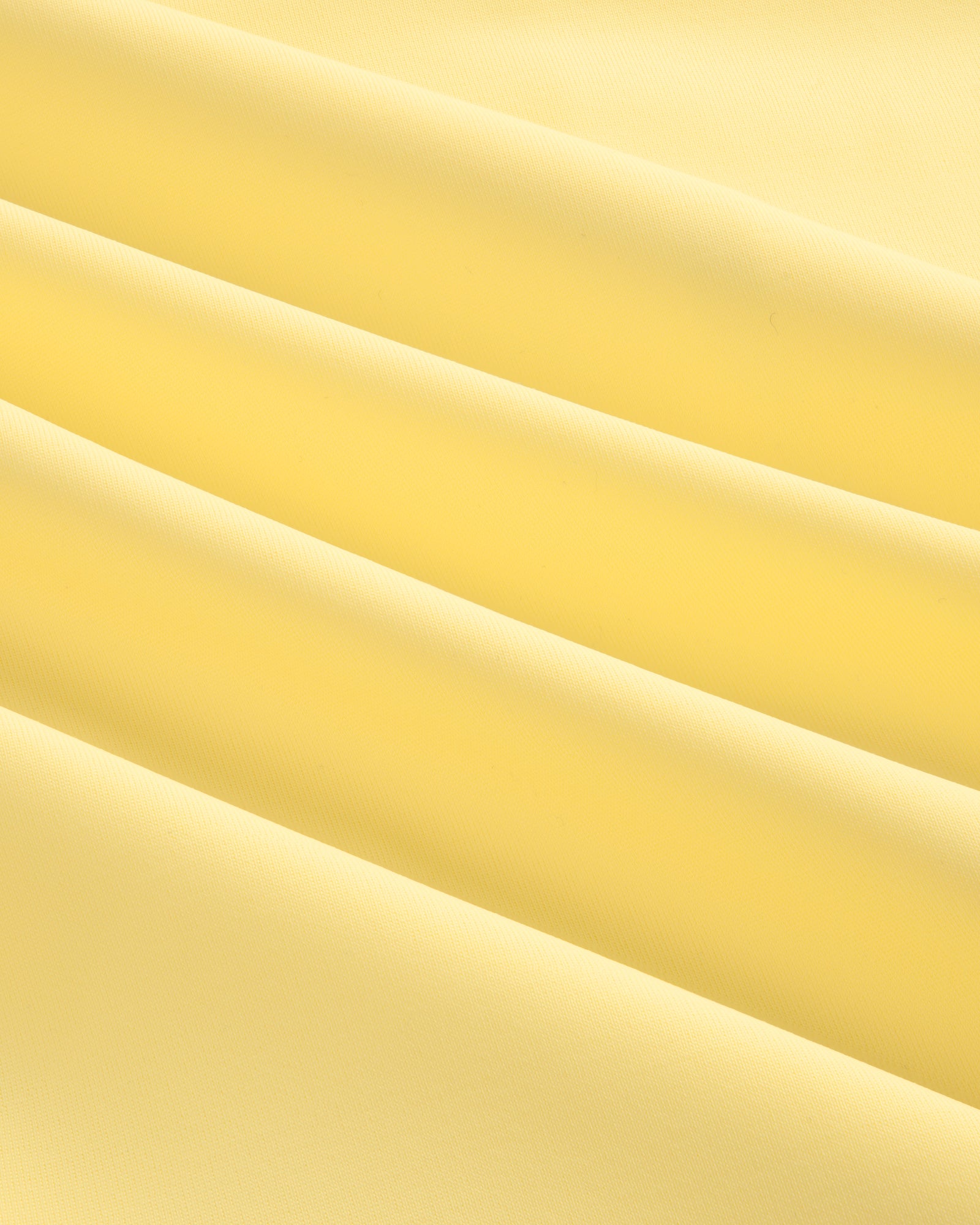 Close-up of soft, smooth light yellow fabric with gentle folds from a Short Sleeve Crest Rash Guard.