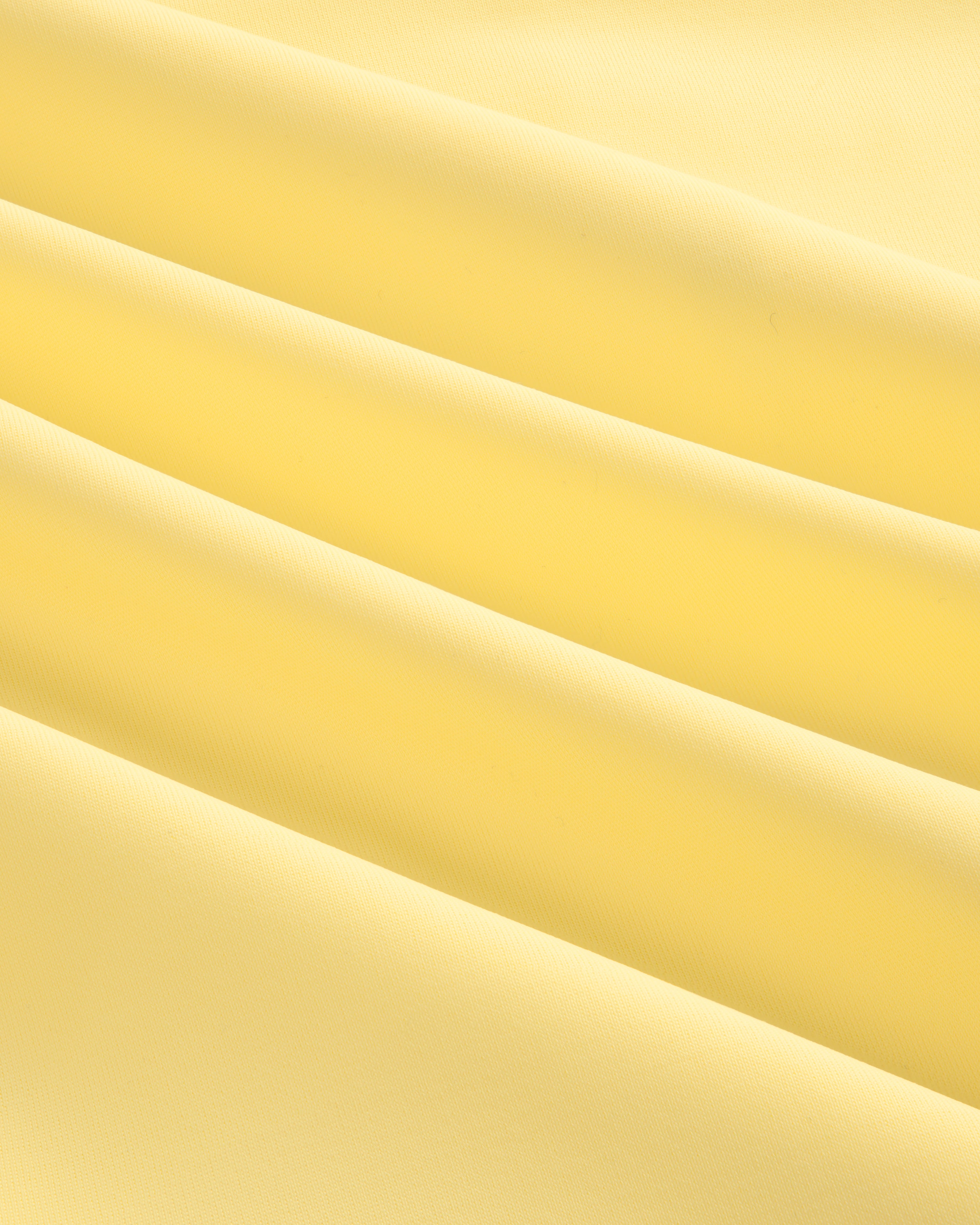 Close-up of soft, smooth light yellow fabric with gentle folds from a Short Sleeve Crest Rash Guard.
