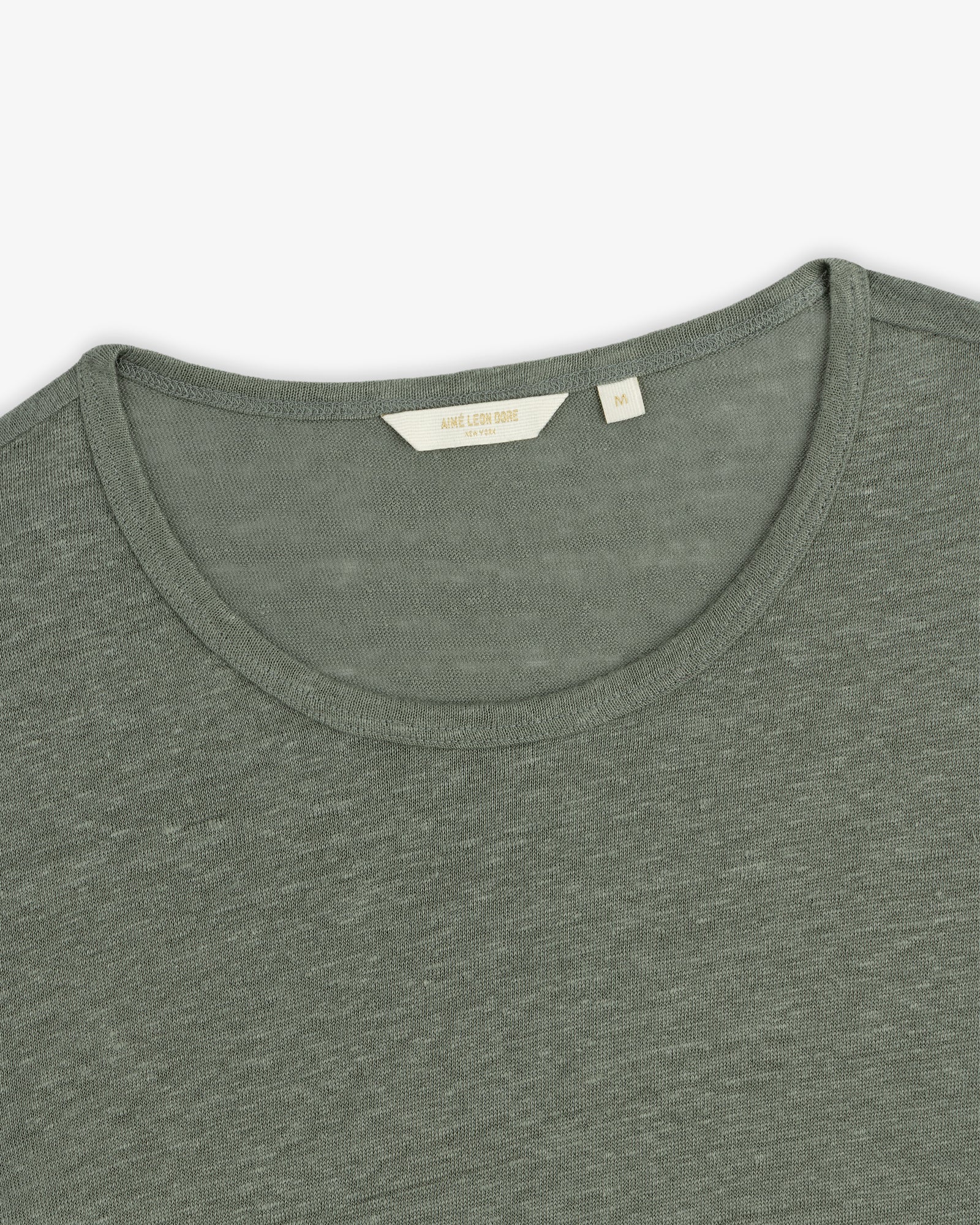 Close-up of the Linen Tee, an olive green crew neck with a visible beige size tag at the collar.