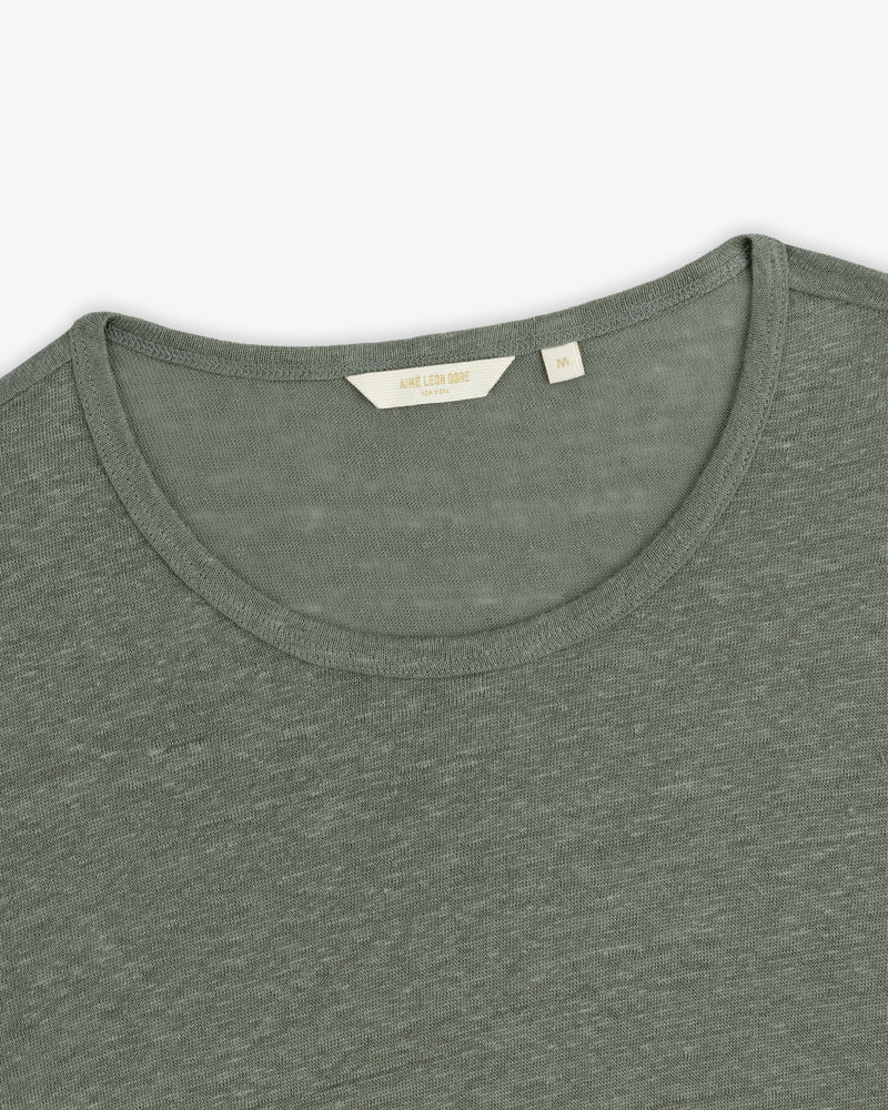 Close-up of the Linen Tee, an olive green crew neck with a visible beige size tag at the collar.