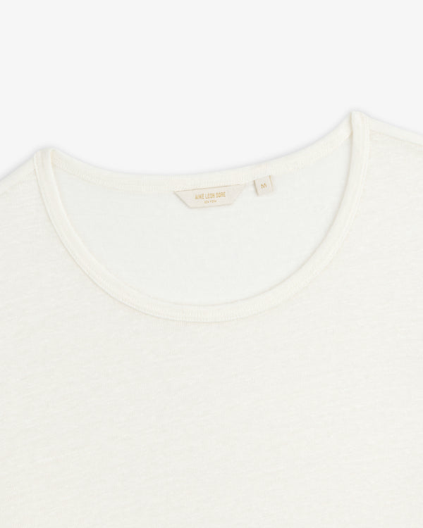Close-up of a white Linen Tee crewneck showing its collar and inner tag with beige text on a plain background.