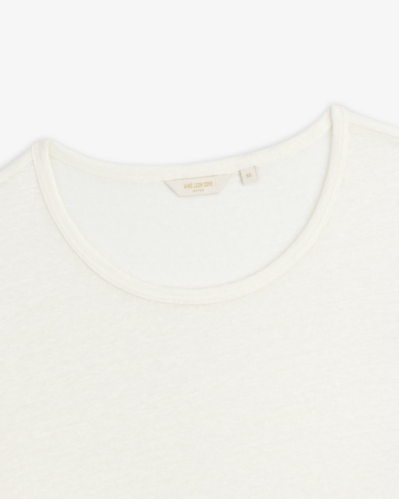 Close-up of a white Linen Tee crewneck showing its collar and inner tag with beige text on a plain background.