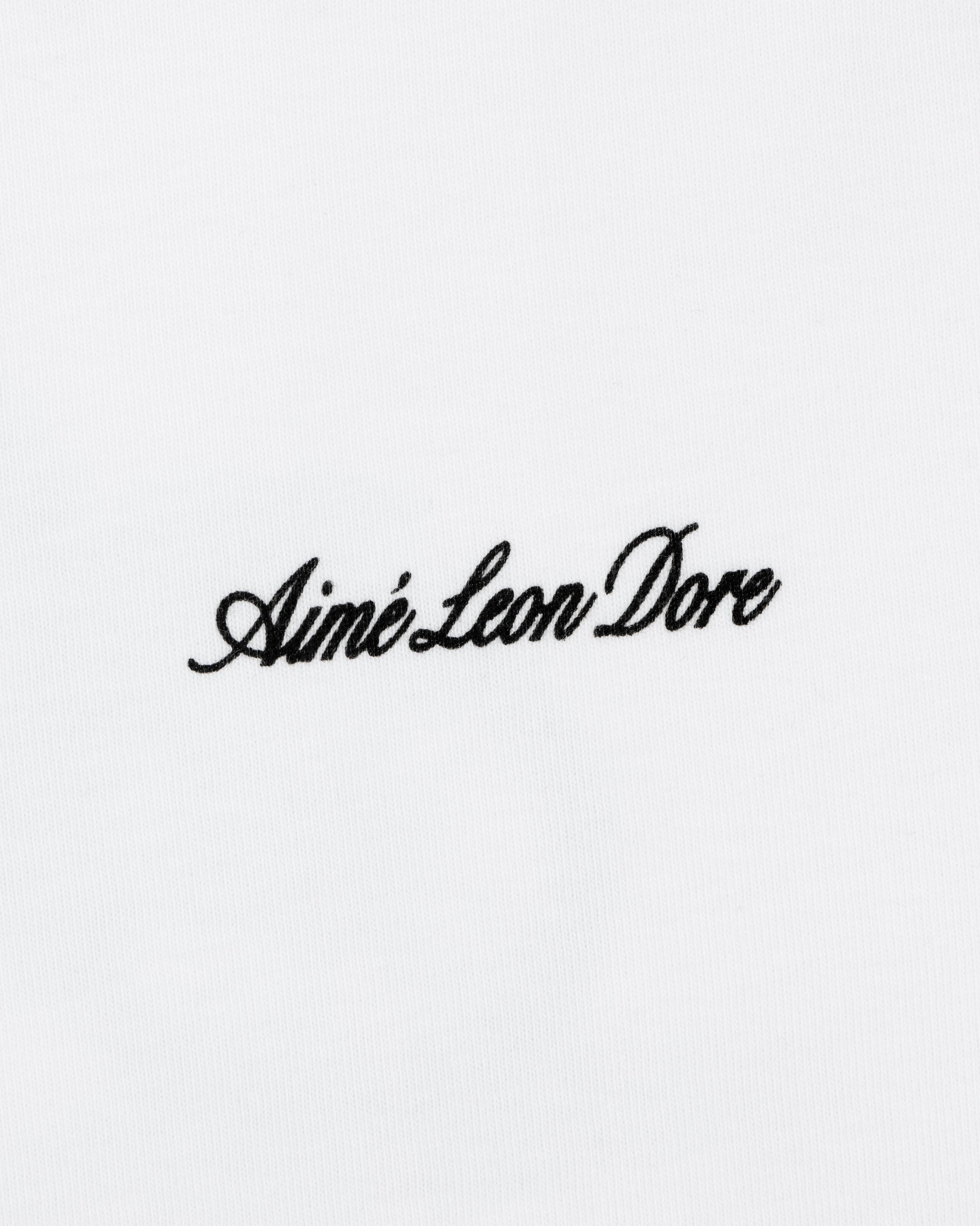 Black script text Aimé Leon Dore is embroidered on the white Super Cub Tee.