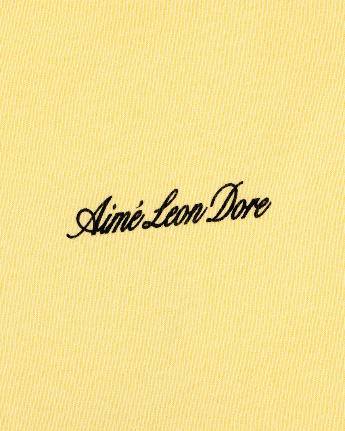 Yellow Super Cub Tee featuring Aimé Leon Dore in black cursive text at the center.