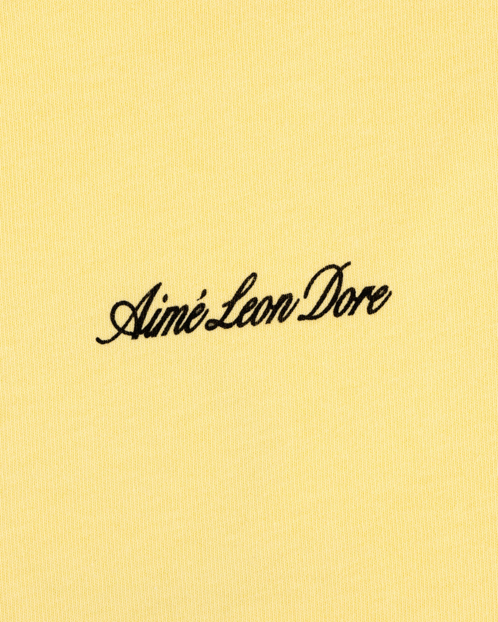 Yellow Super Cub Tee featuring Aimé Leon Dore in black cursive text at the center.