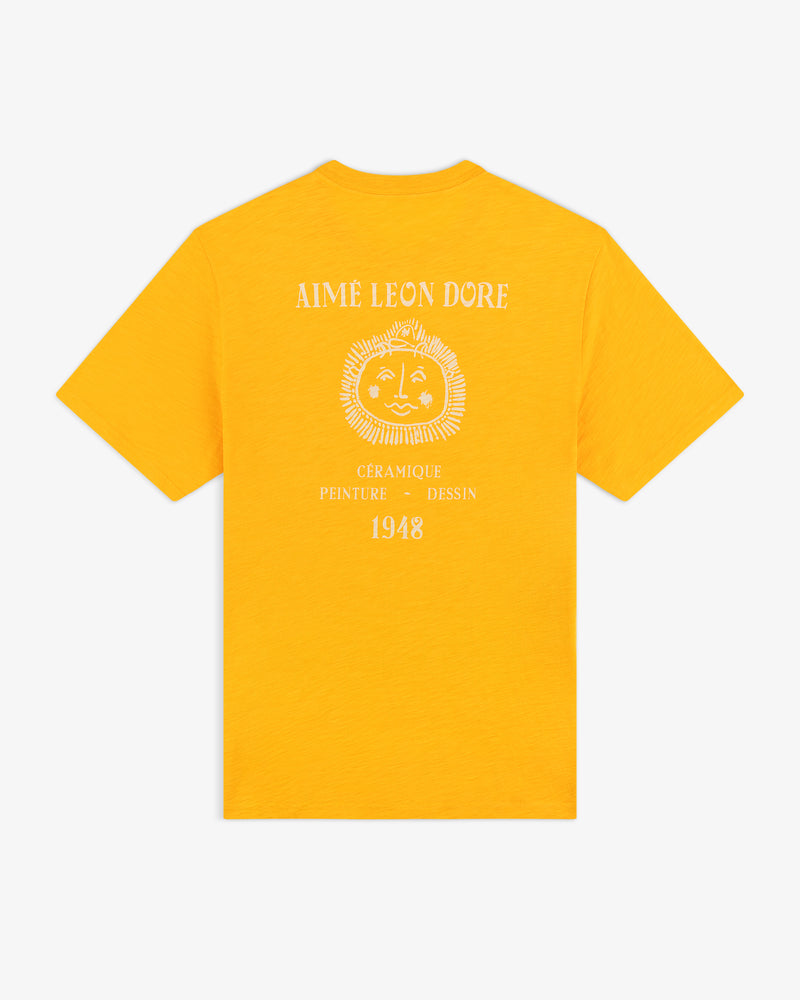 Bright yellow Artiste Pocket Tee with a sun face graphic and "Aime Leon Dore, Céramique, Peinture, Dessin, 1948" on back.
