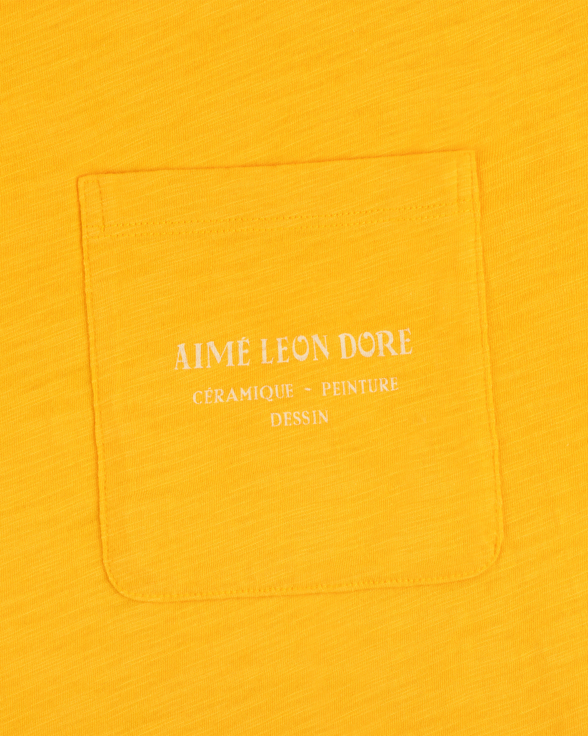 Yellow Artiste Pocket Tee with white text reading AIME LEON DORE CÉRAMIQUE - PEINTURE DESSIN.