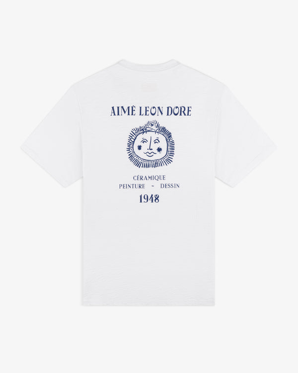 Artiste Pocket Tee: white tee with blue lion graphic and “AIMÉ LEON DORE, CÉRAMIQUE PEINTURE DESSIN 1948” on back.