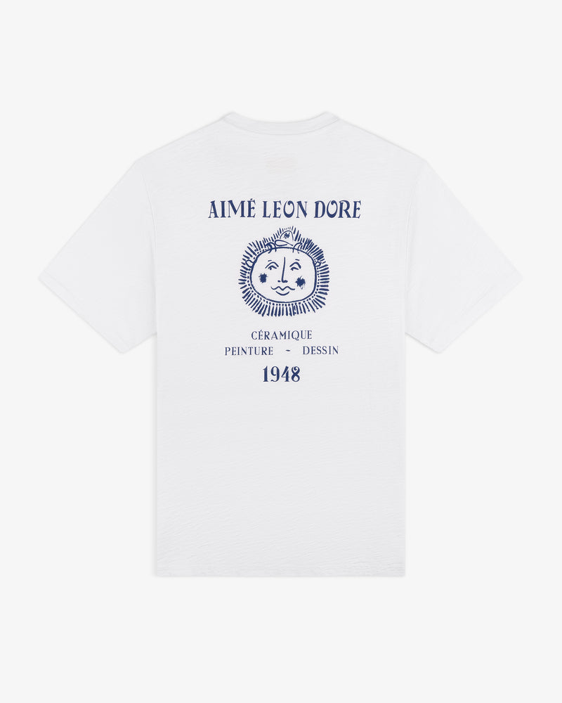 Artiste Pocket Tee: white tee with blue lion graphic and “AIMÉ LEON DORE, CÉRAMIQUE PEINTURE DESSIN 1948” on back.