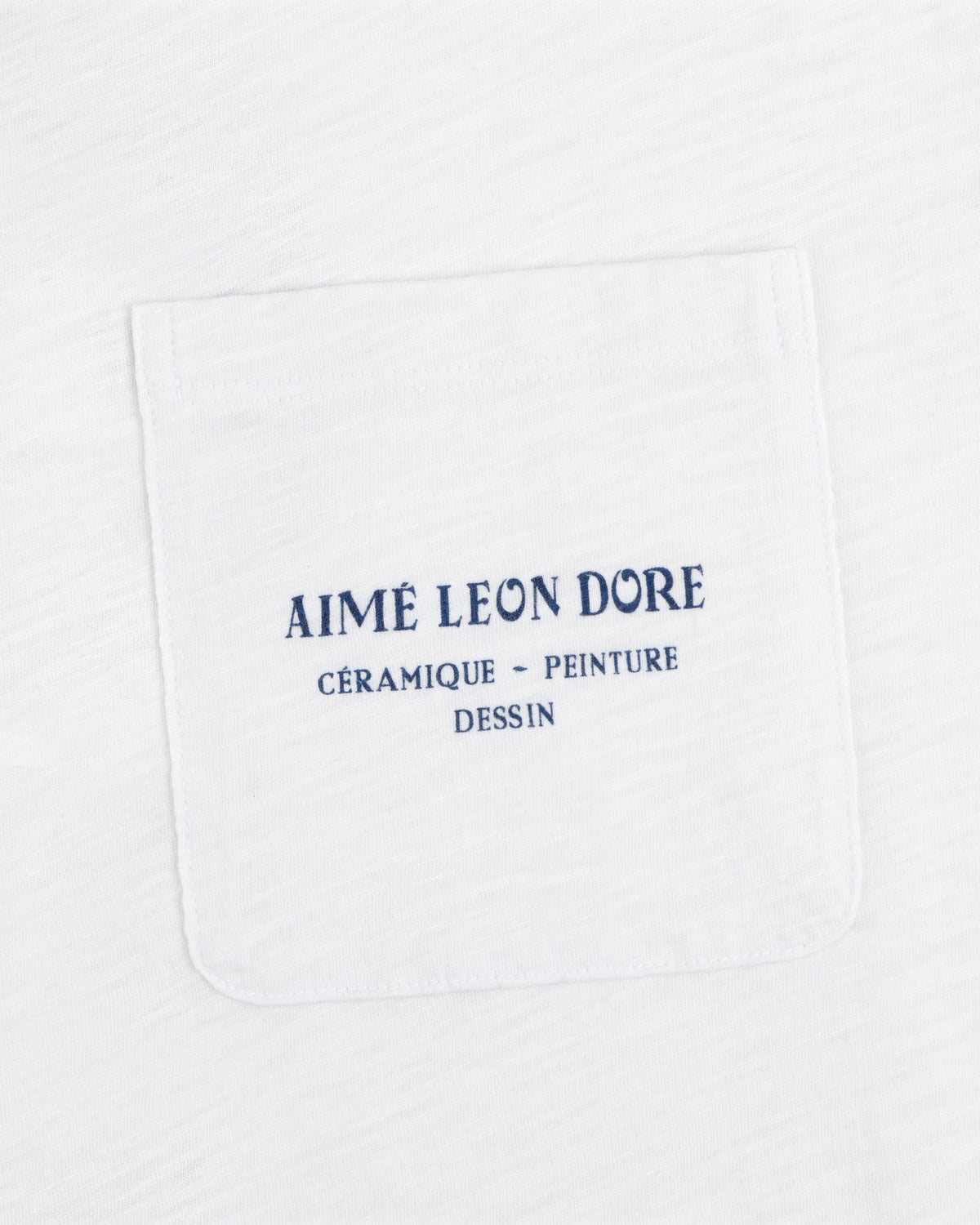Artiste Pocket Tee: White shirt with chest pocket, blue text reads AIMÉ LEON DORE CÉRAMIQUE - PEINTURE DESSIN.