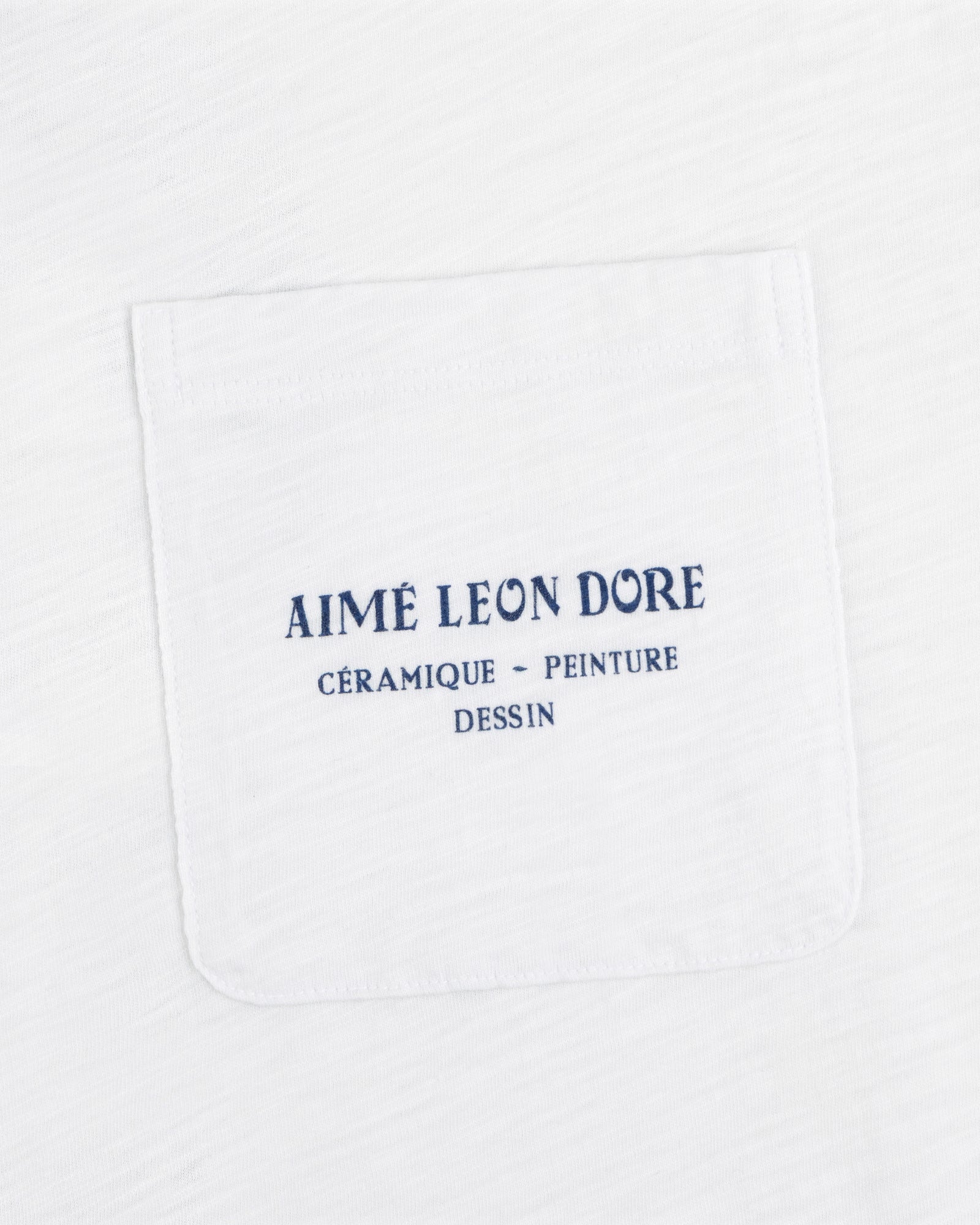 Artiste Pocket Tee: White shirt with chest pocket, blue text reads AIMÉ LEON DORE CÉRAMIQUE - PEINTURE DESSIN.