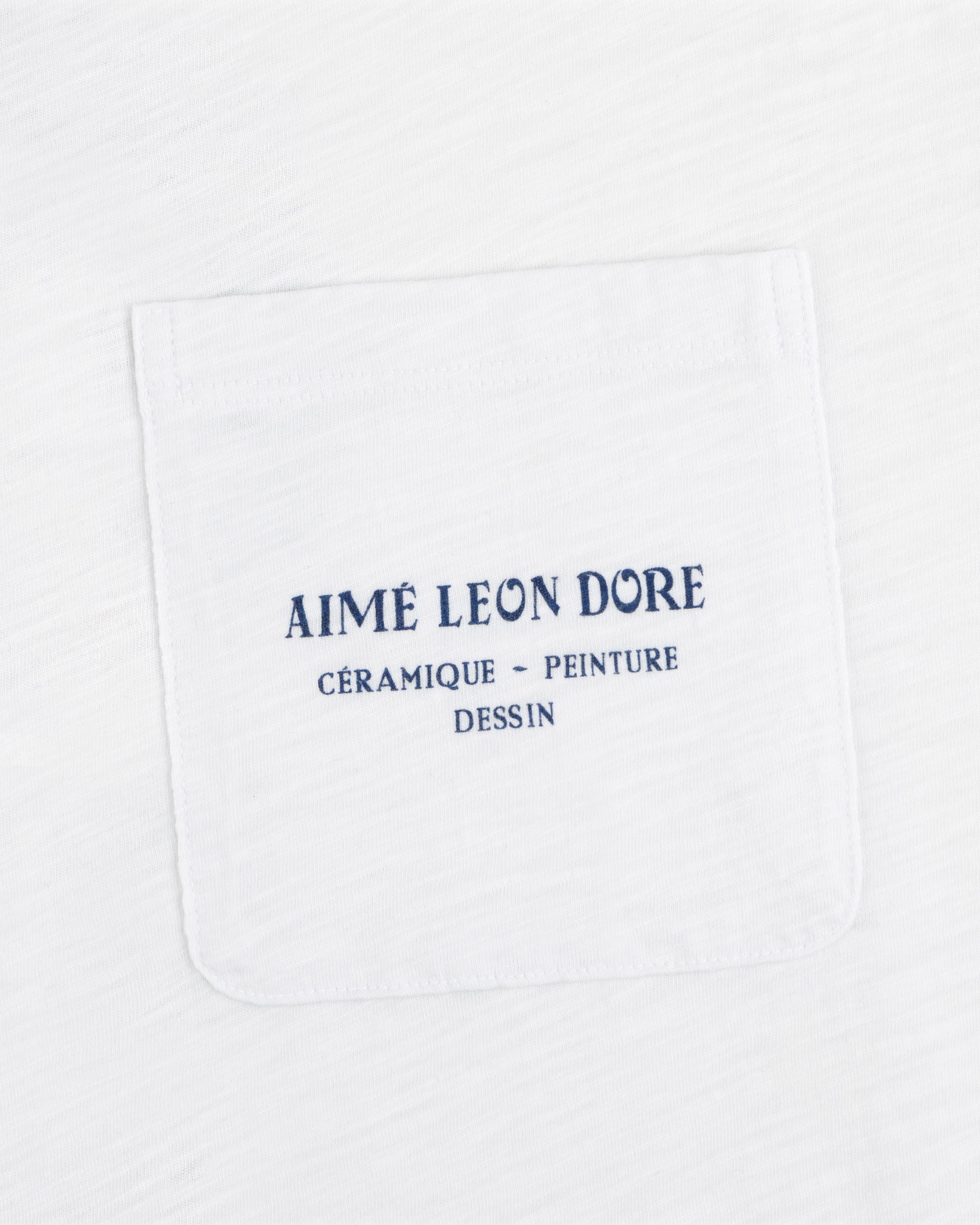 Artiste Pocket Tee: White shirt with chest pocket, blue text reads AIMÉ LEON DORE CÉRAMIQUE - PEINTURE DESSIN.
