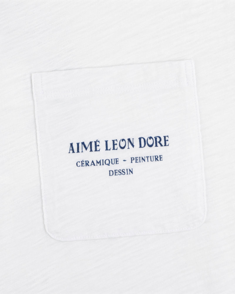 Artiste Pocket Tee: White shirt with chest pocket, blue text reads AIMÉ LEON DORE CÉRAMIQUE - PEINTURE DESSIN.