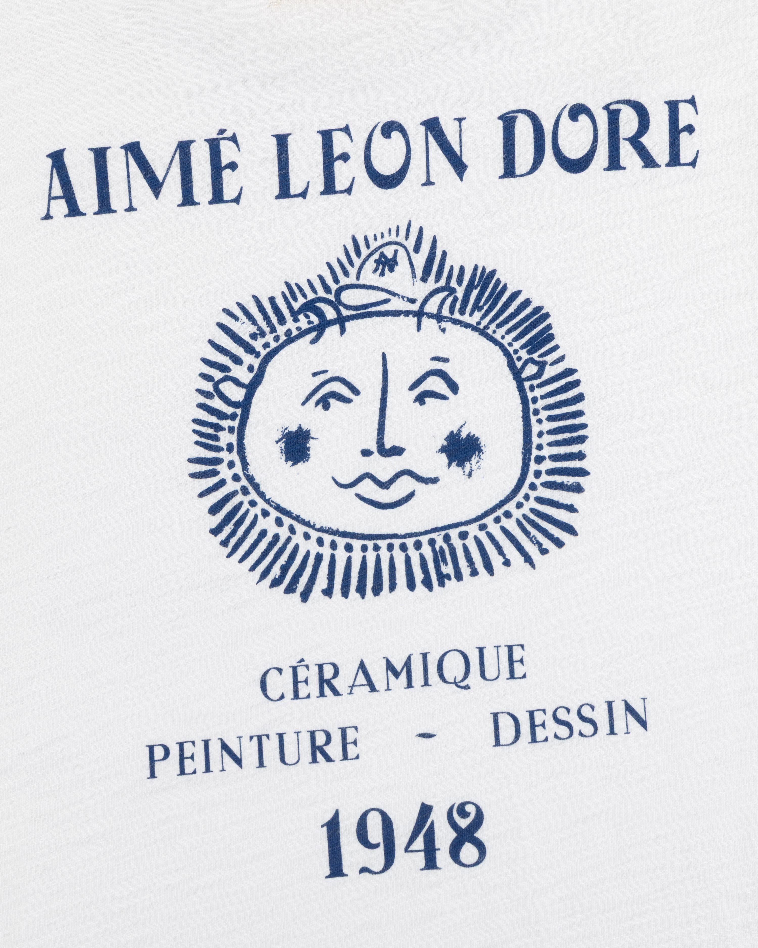 White Artiste Pocket Tee with blue AIMÉ LEON DORE above a sun-face and CÉRAMIQUE PEINTURE DESSIN 1948 text.