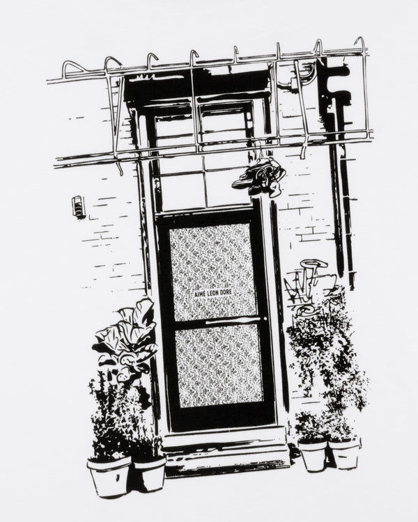 Black and white drawing of a door with potted plants, a fire escape, and "Mott Street Tee" sign above.