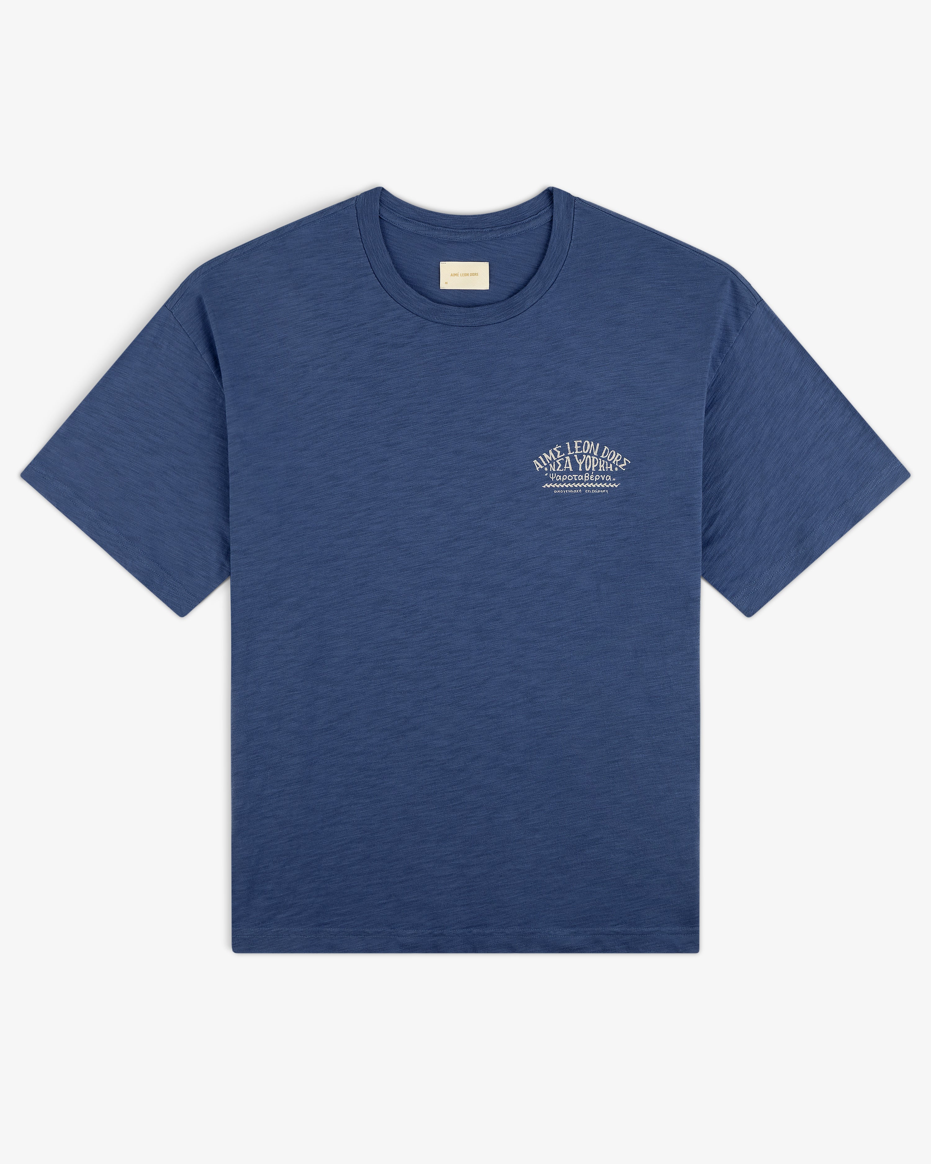 Taverna Tee: Blue short-sleeve t-shirt with small white text graphic on left chest, shown on white background.