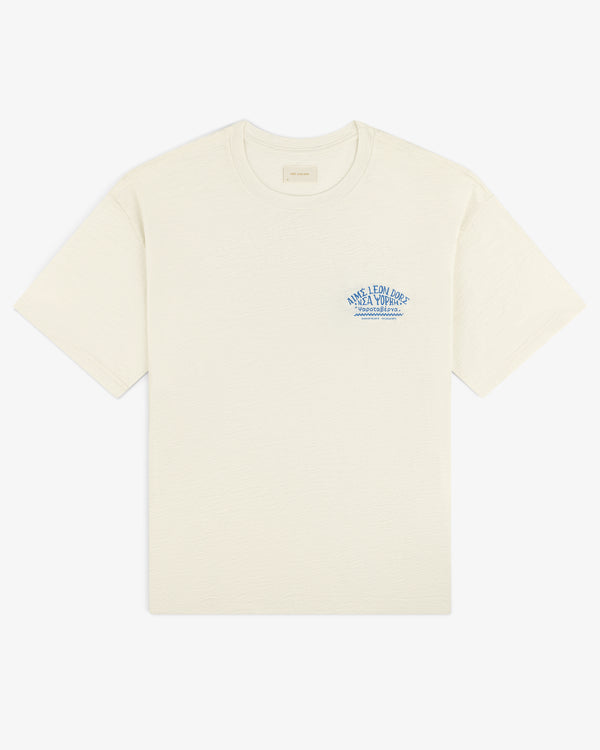 Taverna Tee: Off-white short-sleeve shirt with small blue text and graphic on the left chest.