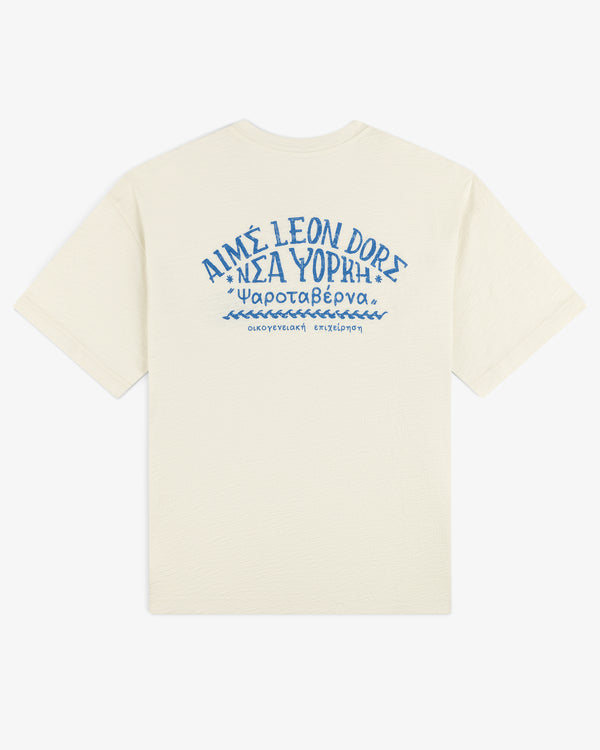 Off-white Taverna Tee with blue Greek text and "AIMÉ LEON DORE" in stylized letters on the back.