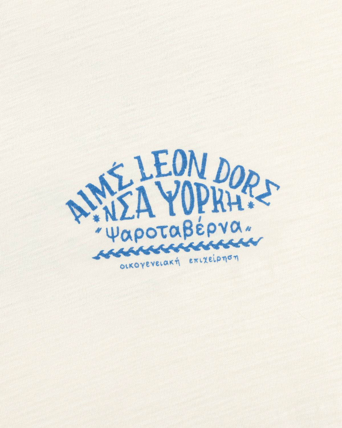 Cream-colored Taverna Tee with blue Greek and English text, including "Aime Leon Dore New York" and Greek words.
