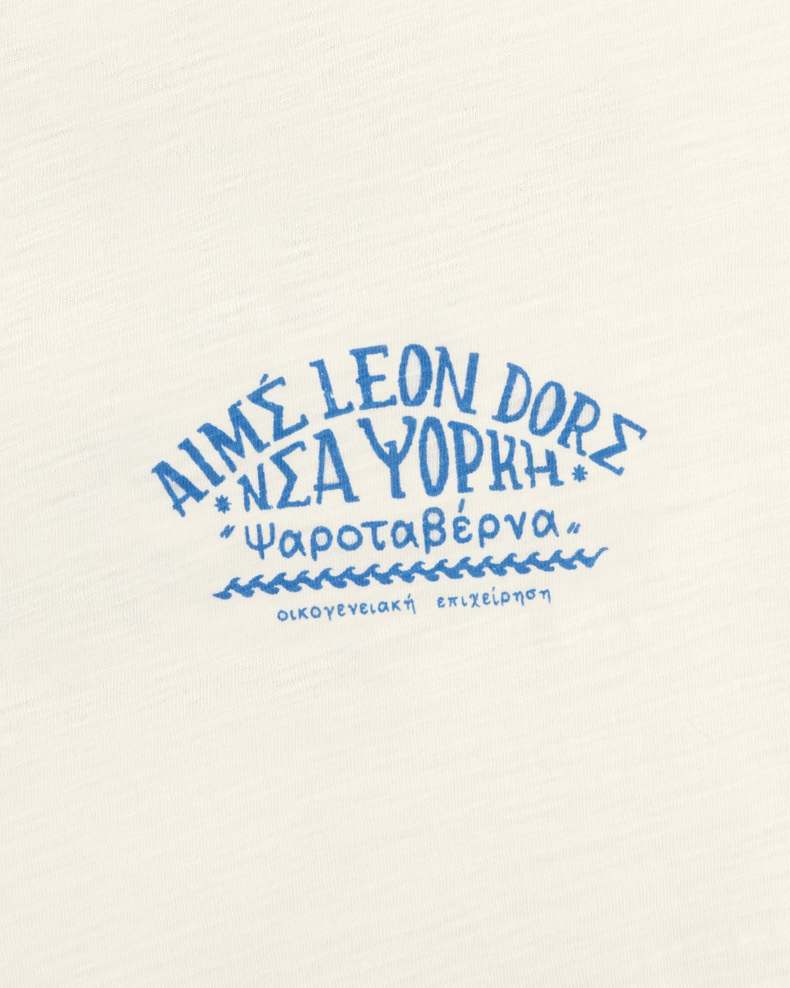 Cream-colored Taverna Tee with blue Greek and English text, including "Aime Leon Dore New York" and Greek words.