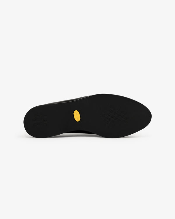 The Venetian Mule’s black sole features a small yellow hexagonal logo in the center, seen from below on white.