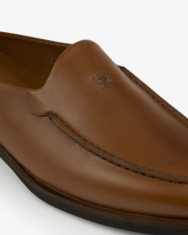 Close-up of the Venetian Mule, a brown leather loafer with visible stitching and a small embossed logo on the upper.