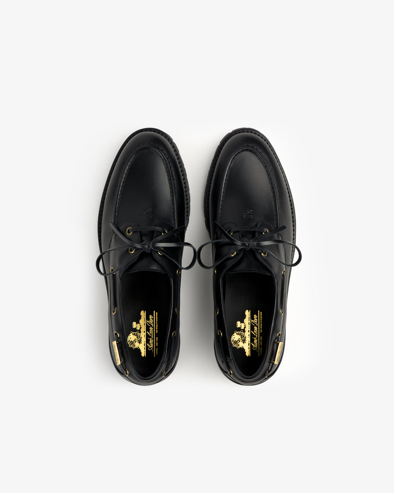 The Pápia Boat Shoe is a black leather lace-up shoe with gold insole branding, shown from above on white.