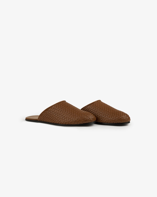 A pair of Leather Raffia Mules with brown woven uppers, closed toes, and flat soles on a white background.