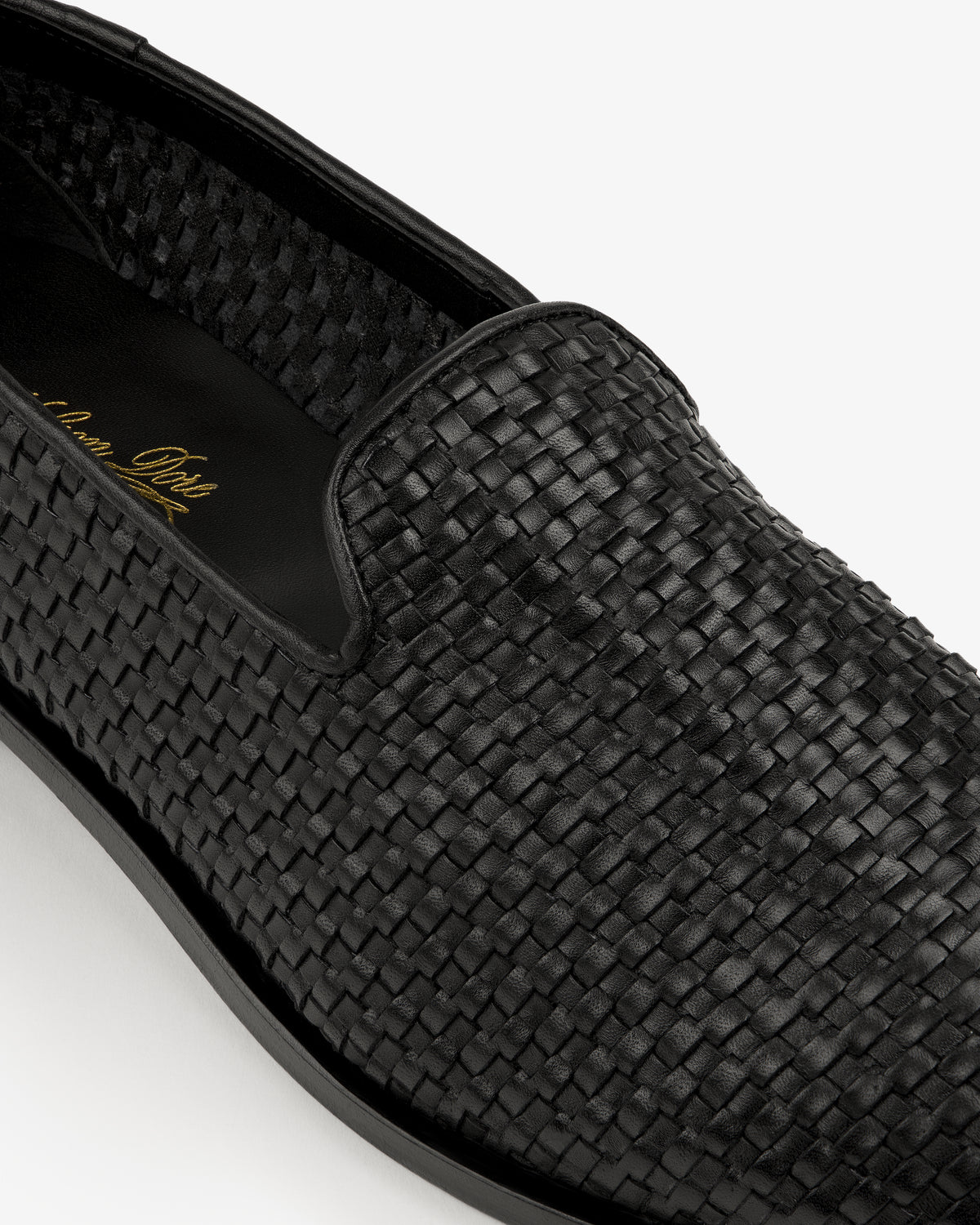 Close-up of the Leather Raffia Loafer, a black woven leather slip-on with rounded toe and black sole.