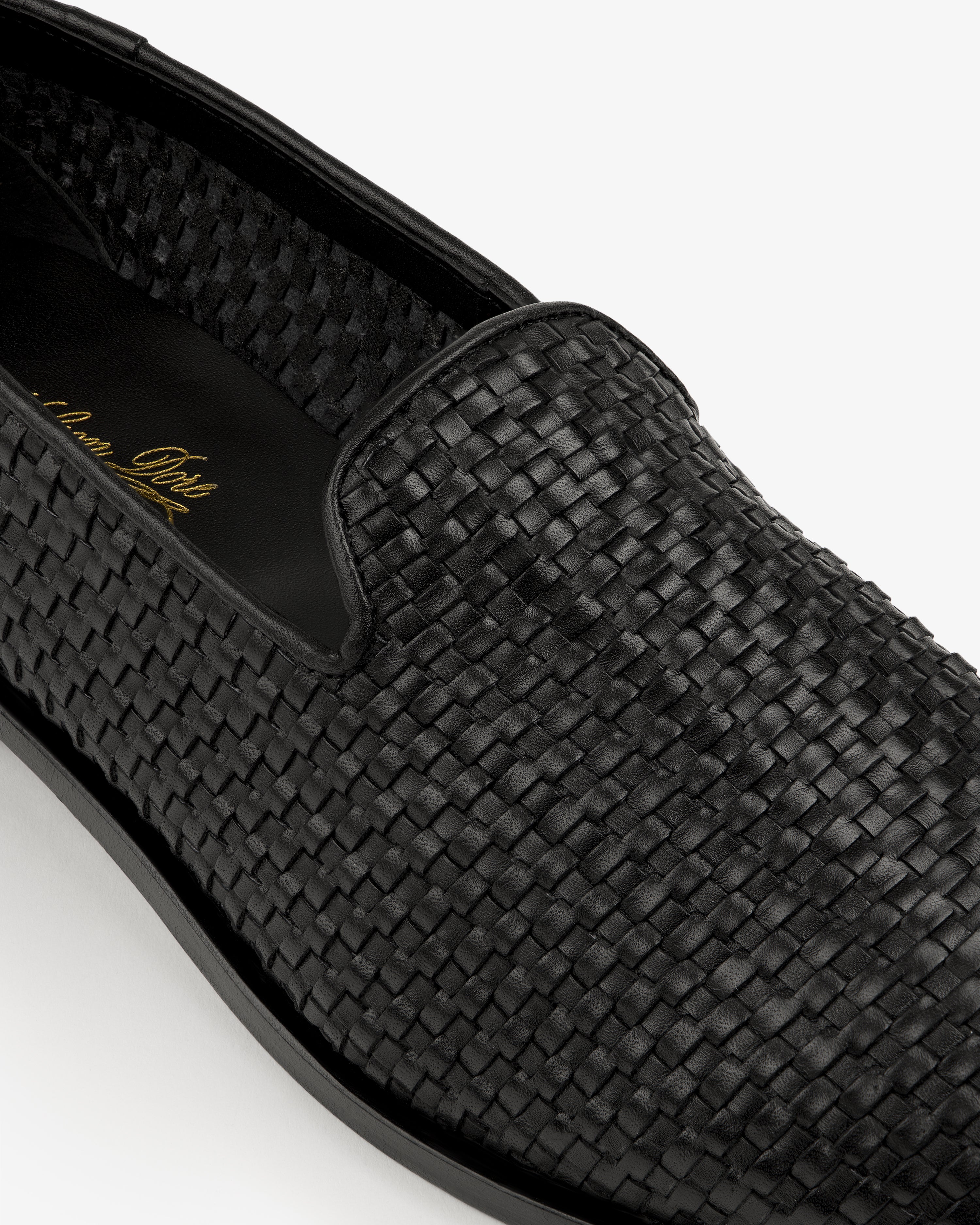 Close-up of the Leather Raffia Loafer, a black woven leather slip-on with rounded toe and black sole.