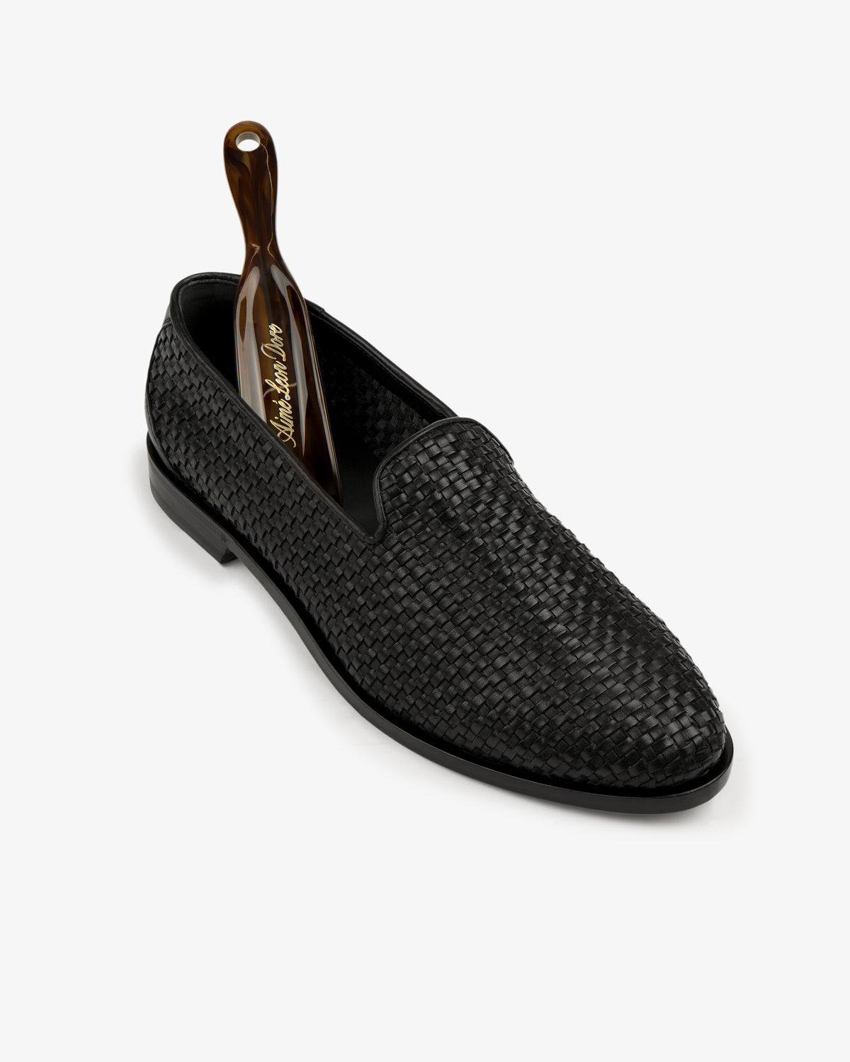Leather Raffia Loafer in black with a brown shoehorn, displayed against a white background.