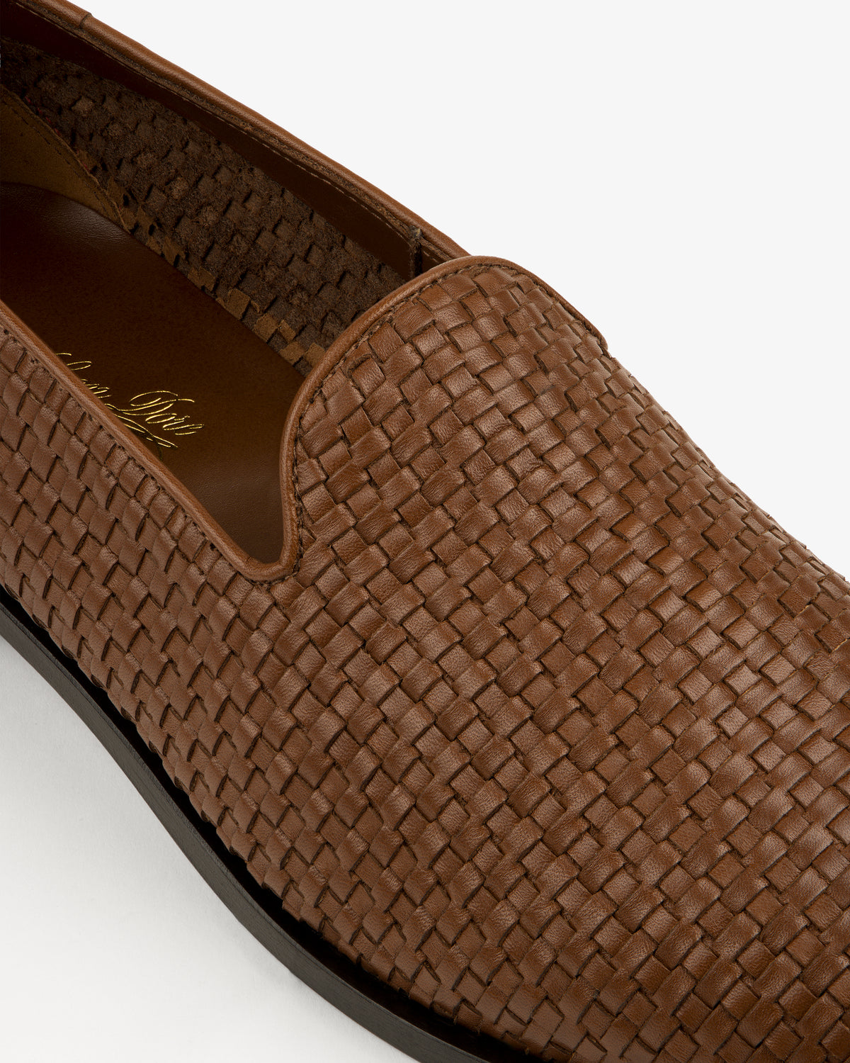 Close-up of the Leather Raffia Loafer in brown woven leather with a black sole on a white background.