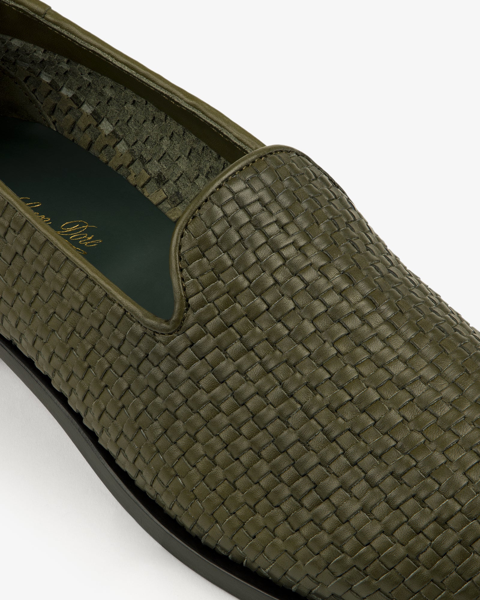 Close-up of a Leather Raffia Loafer in green woven leather with a black sole on a white background.