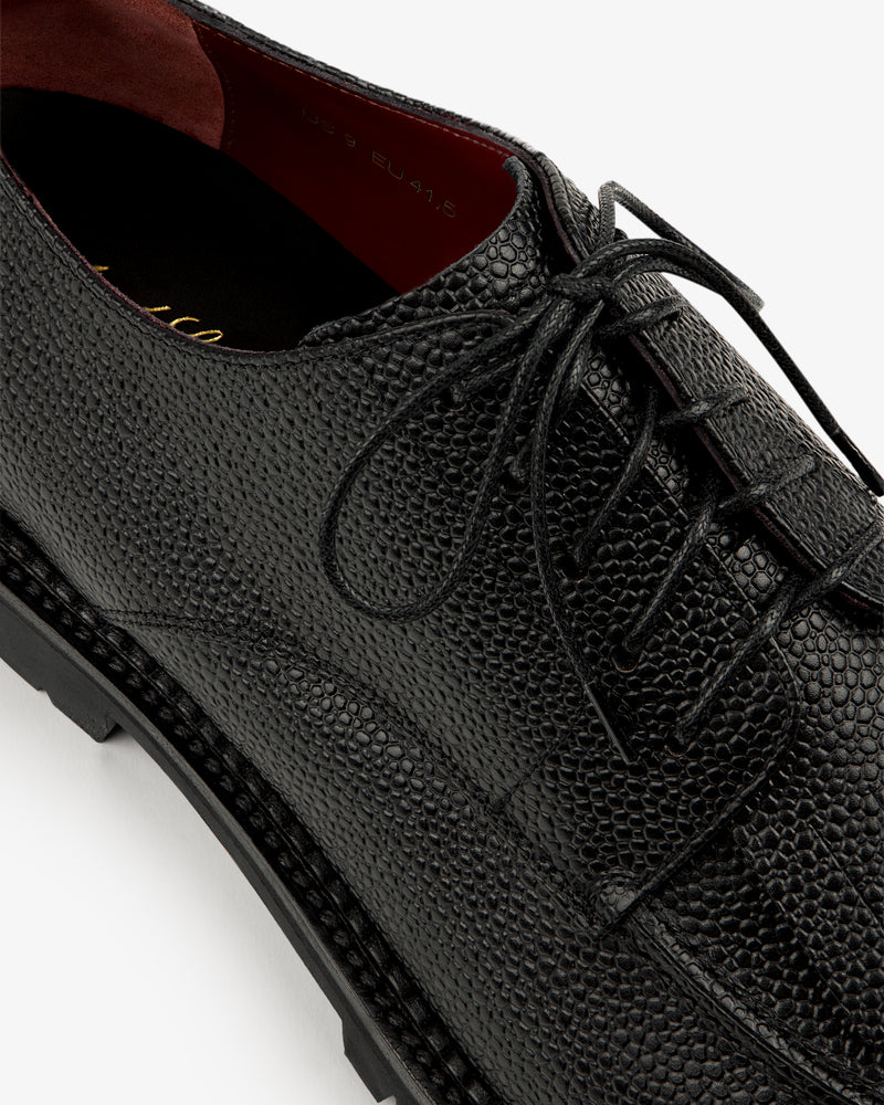 Close-up of the Leather Lug Sole Derby, a black textured leather dress shoe with laces and visible stitching.