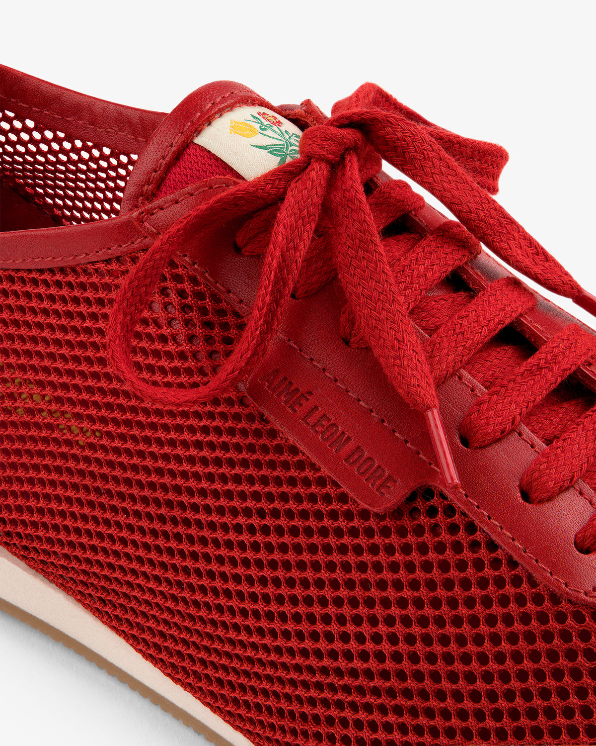 Close-up of the Low Profile Mesh Trainer in red, featuring AIME LEON DORE on the lace tag and a flower on the tongue.
